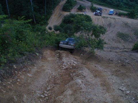 1988 Ford Bronco - A dark SUV navigates a challenging off-road trail, with other vehicles visible further up the path.