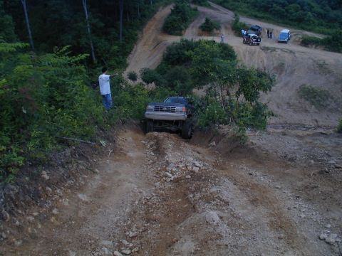 1988 Ford Bronco - Several off-road vehicles traverse a challenging dirt track in a wooded area.