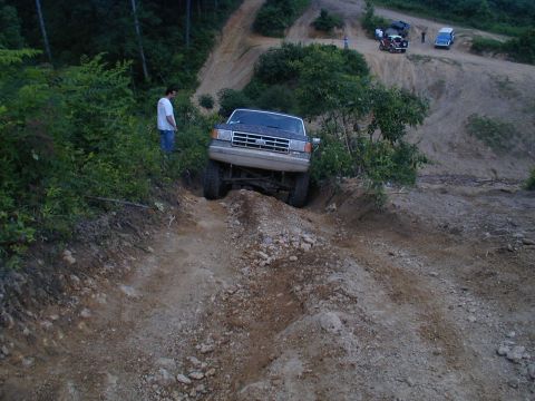 1988 Ford Bronco - A lifted Ford Bronco navigates a challenging off-road trail, with other vehicles and onlookers present.