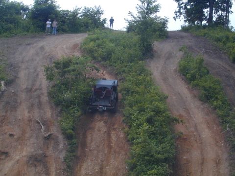 1988 Ford Bronco - A dark SUV navigates a steep, overgrown dirt path with onlookers observing from above.