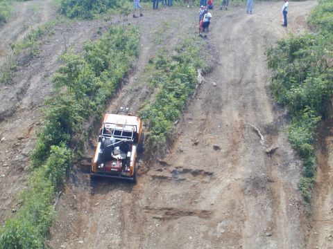 1988 Ford Bronco - An off-road vehicle navigates a challenging, steep incline on a dirt track, with onlookers observing from above.