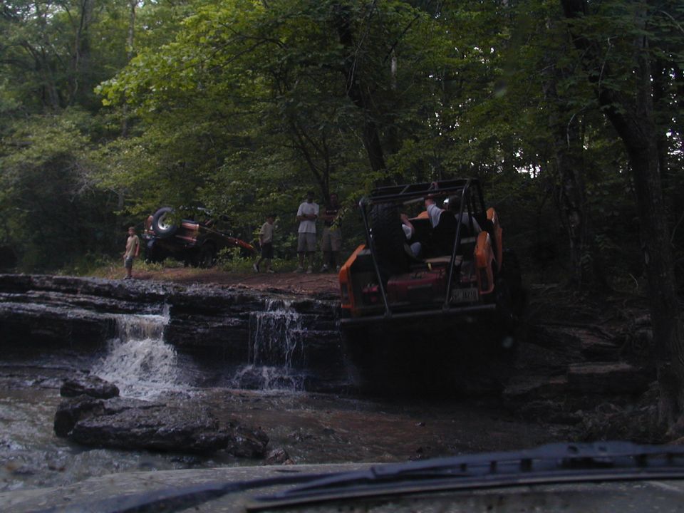 Two off-road vehicles are near a waterfall, one is partially overturned