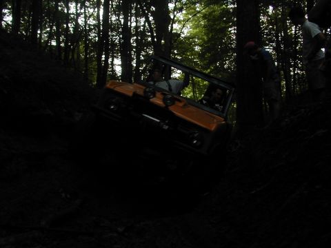 1988 Ford Bronco - An orange off-road vehicle navigates a challenging, steep hill covered in trees.