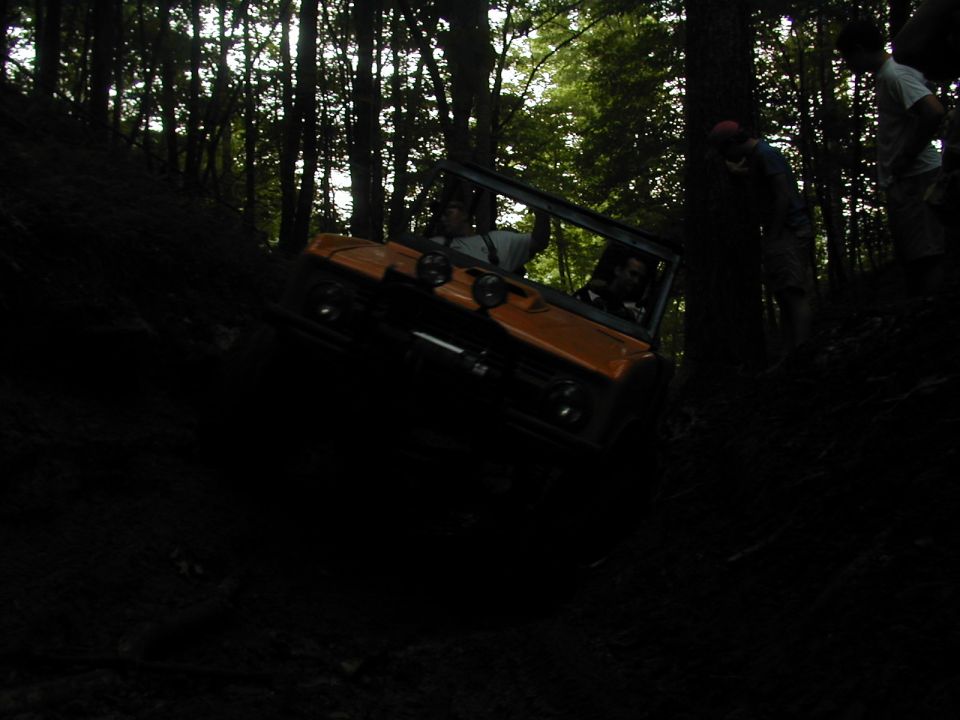 Orange off-road vehicle climbing a steep, wooded incline