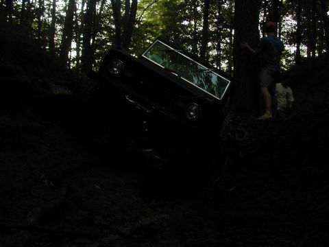 1988 Ford Bronco - A vehicle navigates a steep, wooded terrain with two individuals observing the action.