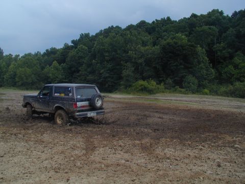 1988 Ford Bronco - Ford Bronco navigates a muddy off-road course under an overcast sky.