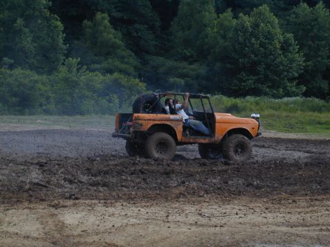 1988 Ford Bronco - An orange off-road vehicle navigates a muddy terrain with trees in the background.