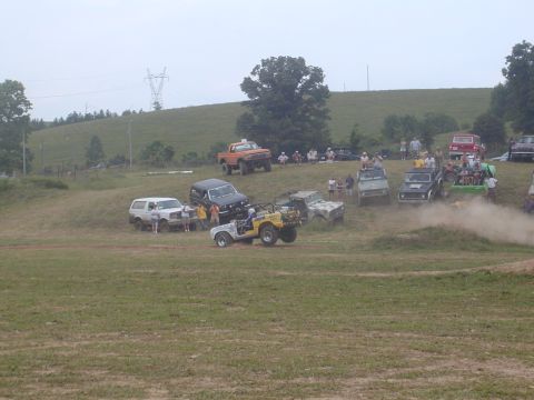 1988 Ford Bronco - Multiple off-road vehicles are gathered on a grassy hill, with spectators in the background.