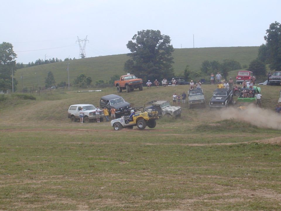 Off-road vehicles gathered on a grassy hill with spectators watching