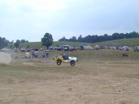 1988 Ford Bronco - An off-road vehicle soars through the air during an event, with a crowd gathered on the hillside.