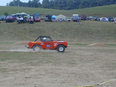 1988 Ford Bronco - Orange Ford Bronco with roll cage kicks up dust while driving on a dirt track during an event.