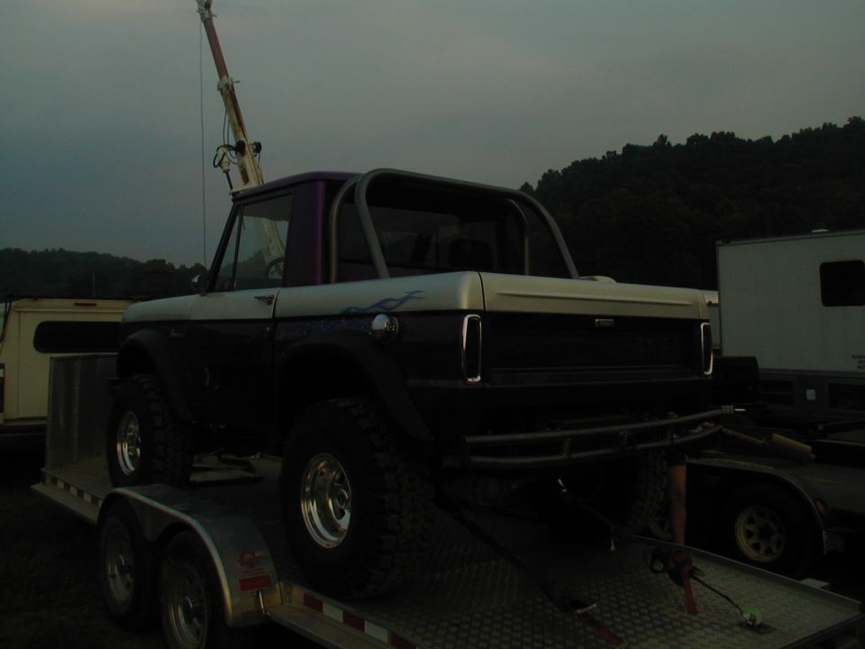 Purple and white flamed early Bronco half-cab with roll cage on a flatbed trailer at dusk