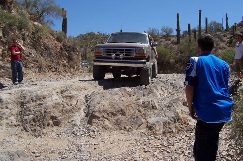1992 Ford Bronco - A brown SUV navigates a challenging rocky path in a desert landscape with saguaro cacti.