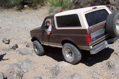 1992 Ford Bronco - A brown 1992 Ford Bronco with a beige top navigates a rocky off-road path.