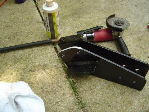 1986 Ford Bronco - A freshly painted black steel bracket or mounting plate with multiple bolt holes lies on a concrete surface, alongside a red pneumatic angl…