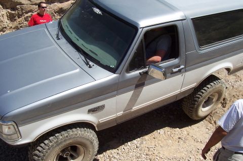 1992 Ford Bronco - A two-tone Ford Bronco navigates a rocky, off-road path with a person in the driver's seat.