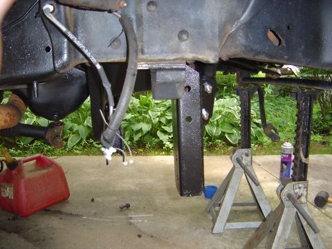 1986 Ford Bronco - View under a raised truck frame painted black, with a lift-style drop bracket freshly bolted to the crossmember and disconnected brake line…