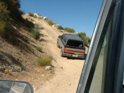 1990 Ford Bronco - A Ford Bronco navigates a dusty, off-road trail under a clear blue sky.