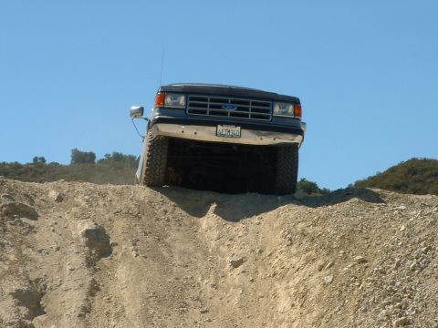 1990 Ford Bronco - A 1990 Ford Bronco navigates a steep, rocky incline under a clear blue sky.