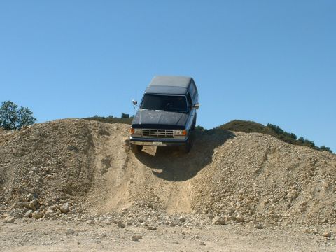 1990 Ford Bronco - A Ford Bronco navigates a steep, rocky incline under a clear blue sky.