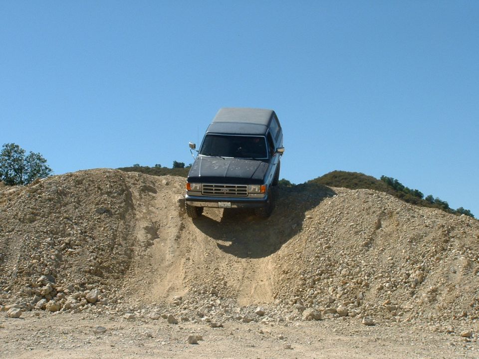 Dark blue Ford Bronco driving up a dirt hill. It's a 1987 model