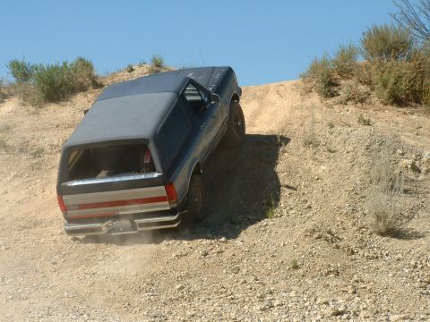 1990 Ford Bronco - A 1990 Ford Bronco navigates an off-road dirt incline under a clear blue sky.