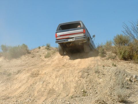1990 Ford Bronco - A 1990 Ford Bronco navigates a challenging dirt incline, kicking up dust as it ascends.