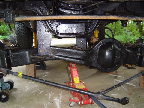1986 Ford Bronco - Underside view of a lifted 4x4 showing the black-painted front solid axle housing, differential, tie rod and track bar, with the vehicle su…