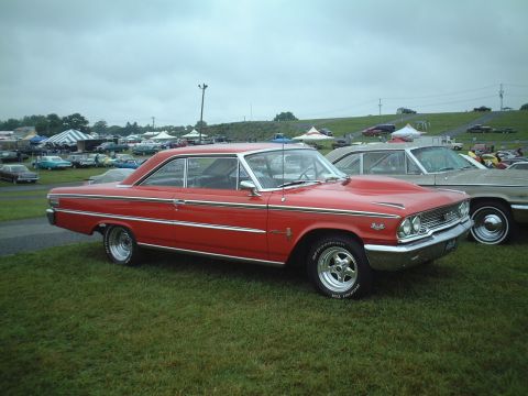 1967 Ford Galaxie - A red 1963 Ford Galaxie 500 with a prominent hood scoop is displayed at an outdoor car show.