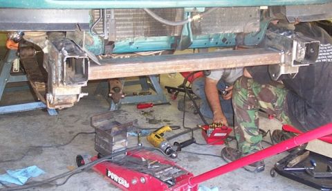 1990 Ford Bronco - Mechanics work on a vehicle's frame, possibly for a custom modification.