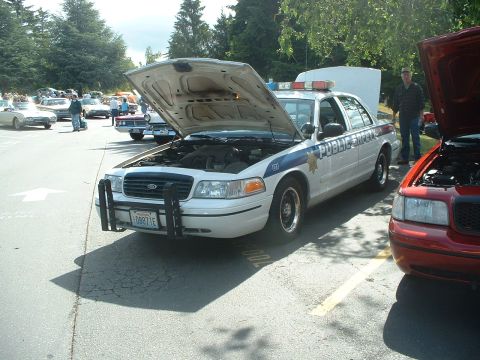 1999 Ford Crown Victoria - A 1999 Ford Crown Victoria police car is displayed with its hood open at an outdoor car show.