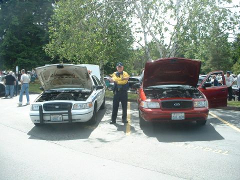 1999 Ford Crown Victoria - Two Ford Crown Victoria police cars are displayed with their hoods open at an outdoor event.