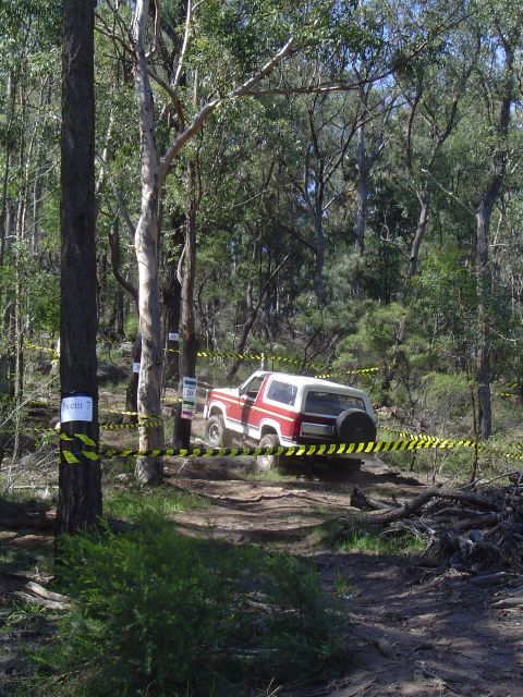 1982 Ford Bronco - An off-road vehicle is shown on a trail, marked by caution tape, within a dense forest environment.