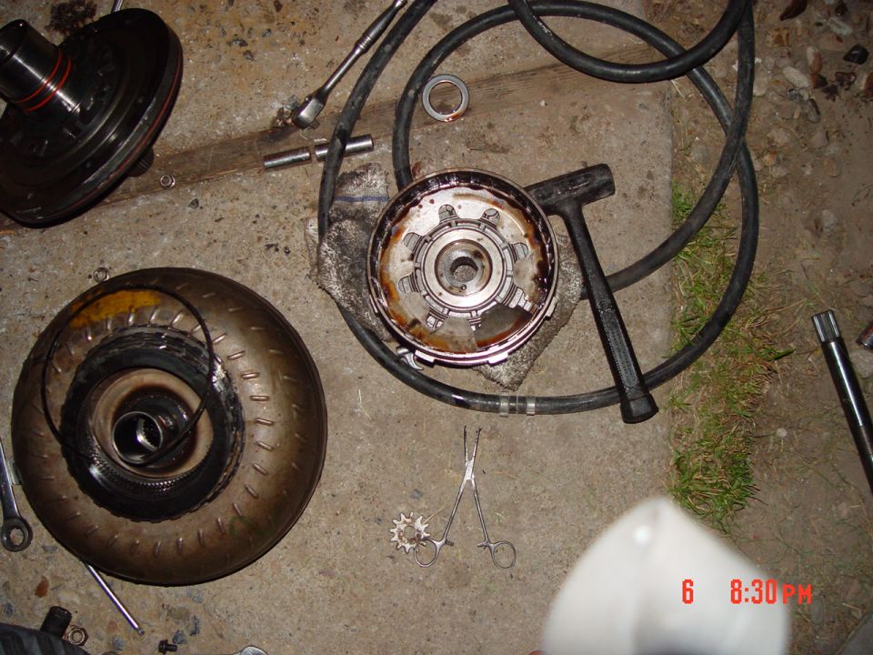 Disassembled automatic transmission parts on a garage floor with torque converter and tools