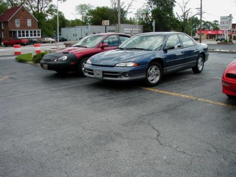 1997 Ford Taurus - Three cars parked in a lot, one blue sedan in the foreground.