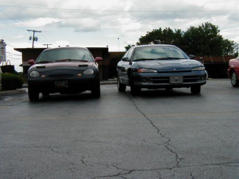 1997 Ford Taurus - Two cars are parked in a lot under a cloudy sky. The blue car on the right appears to be a 1997 Dodge Intrepid.