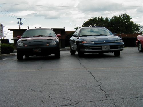 Two cars parked in a lot, one dark colored and one blue. The blue car is a 1997 Dodge Intrepid