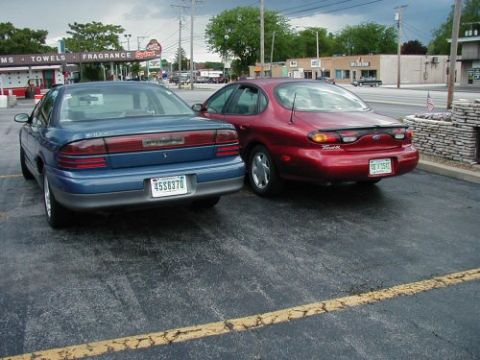 1997 Ford Taurus - Two sedans, one a red 1997 Ford Taurus, are parked in an outdoor lot.