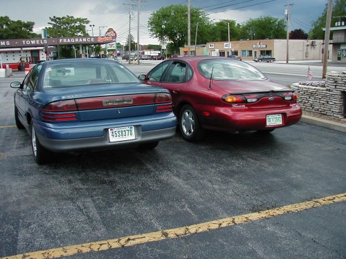 Red 1997 Ford Taurus parked next to a blue sedan, rear view