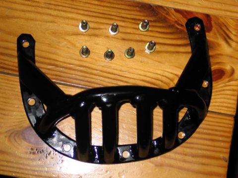 1995 Ford Bronco - A black metal grille piece and several bolts are laid out on a wooden surface.
