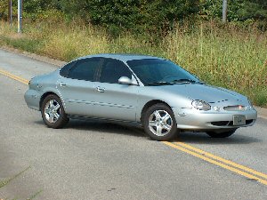 1998 Ford Taurus - A silver 1998 Ford Taurus sedan is parked on the side of a road, captured from a 3/4 front angle.