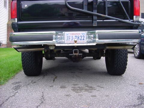 1989 Ford Bronco - The rear view of a black pickup truck shows its chrome bumper, hitch receiver, and dual exhaust system.