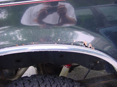 1989 Ford Bronco - Rust is visible on the fender above the wheel well and chrome trim of a dark green vehicle.
