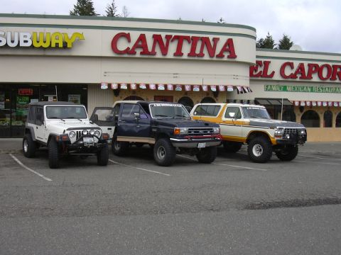 1991 Ford Bronco - Three modified SUVs, including a 1978 Ford Bronco, parked in front of a Cantina restaurant.