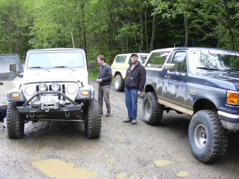 1991 Ford Bronco - A group of off-road vehicles are parked on a muddy trail.