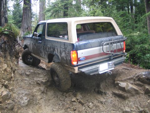 1991 Ford Bronco - Ford Bronco tackling a challenging muddy and rocky off-road path in a wooded area.