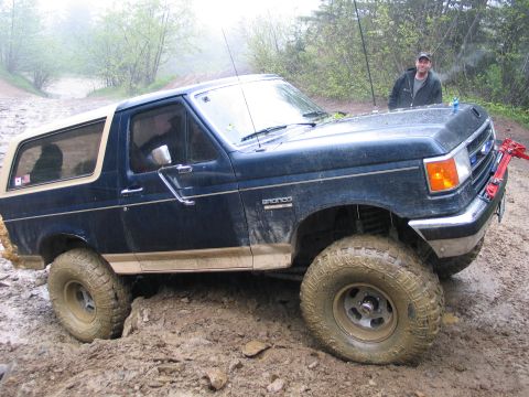 1991 Ford Bronco - Ford Bronco navigating a muddy trail with a person standing behind it.