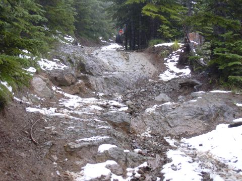 1991 Ford Bronco - An off-road vehicle navigates a challenging, rocky path with patches of snow in a forested mountain area.