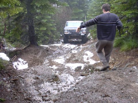 1991 Ford Bronco - A 1991 Ford Bronco navigates a challenging muddy and snowy path through a dense forest.