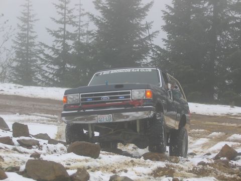 1991 Ford Bronco - A dark blue Ford Bronco navigates a challenging off-road course covered in snow and rocks.